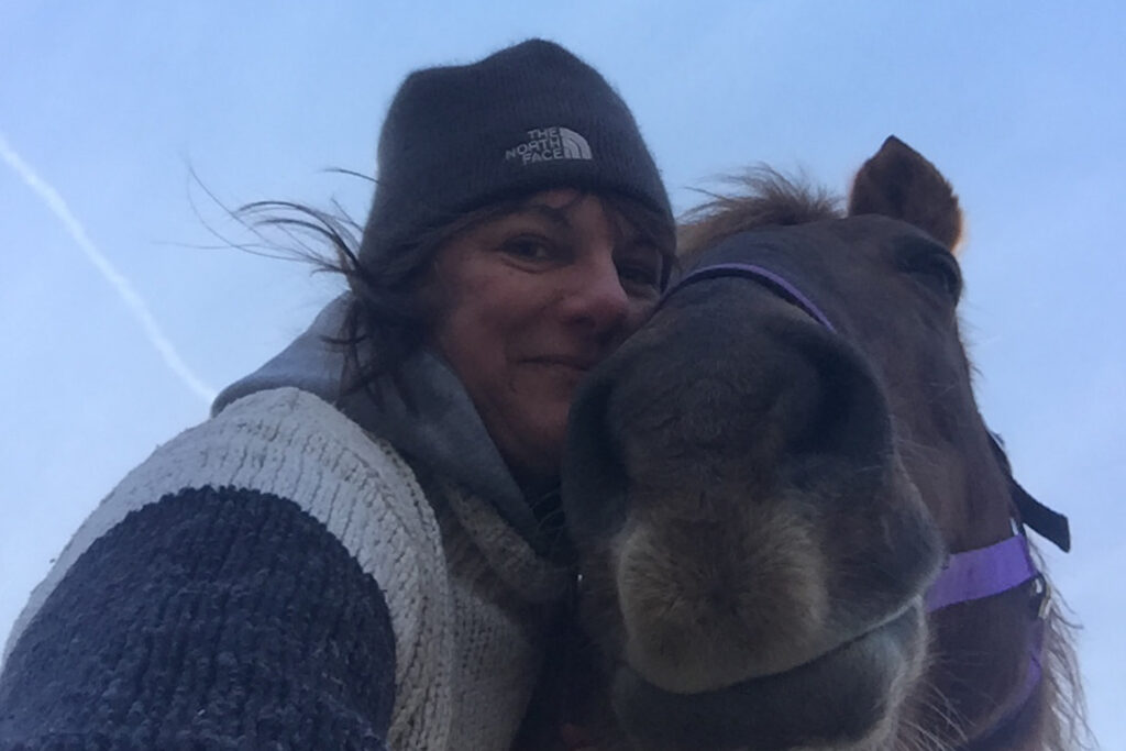 head shot of woman with hat and sweater hugging horse