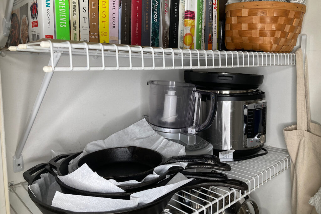 cast iron pans stacked in pantry with cookbooks and instapot