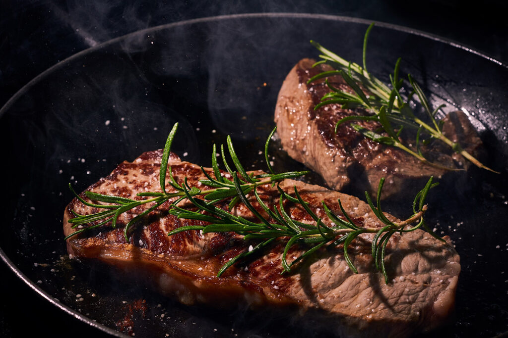 steak in cast iron skillet with rosemary garnish