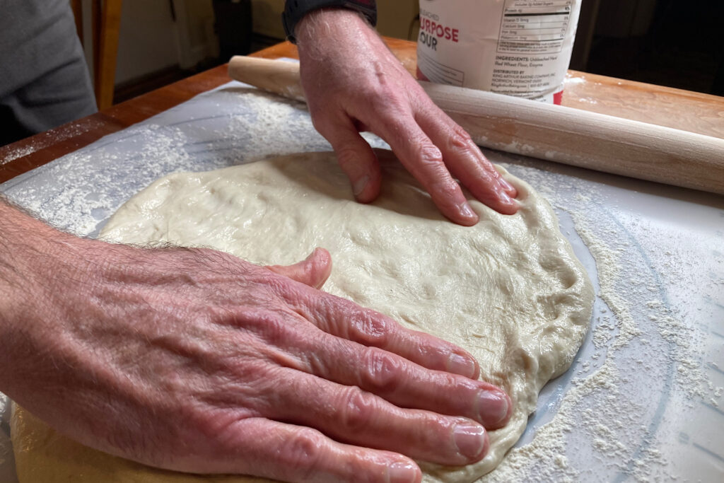 pressing out pizza dough on rolling mat