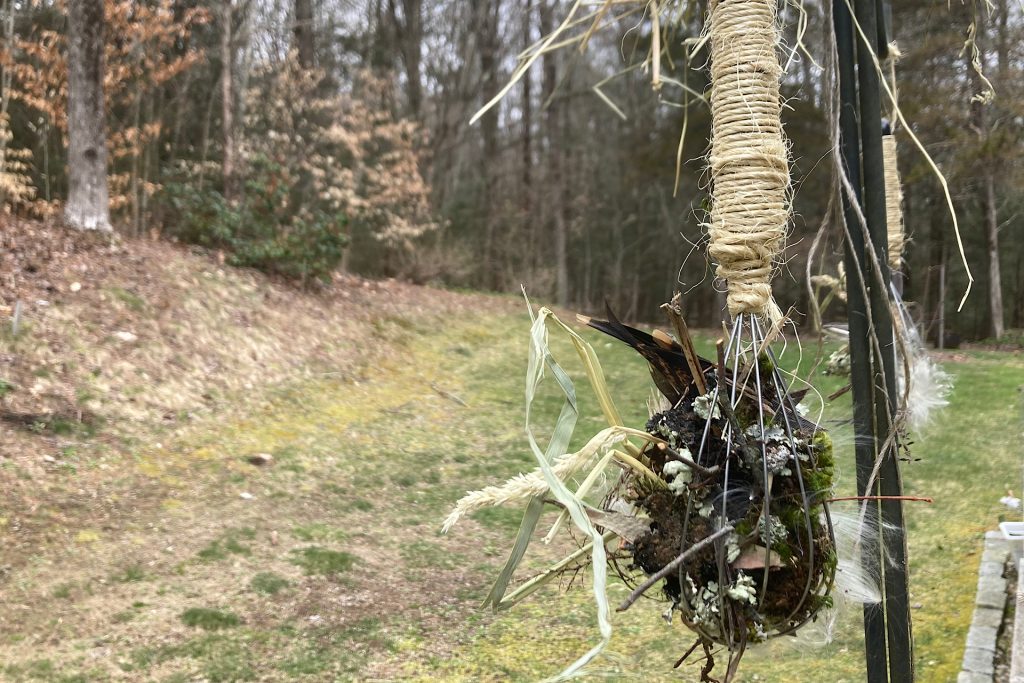 whisk hung outdoors with nesting material for birds