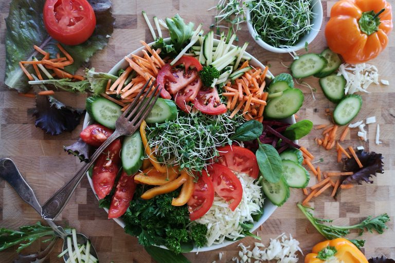 fresh salad in bowl surrounded by vegetables