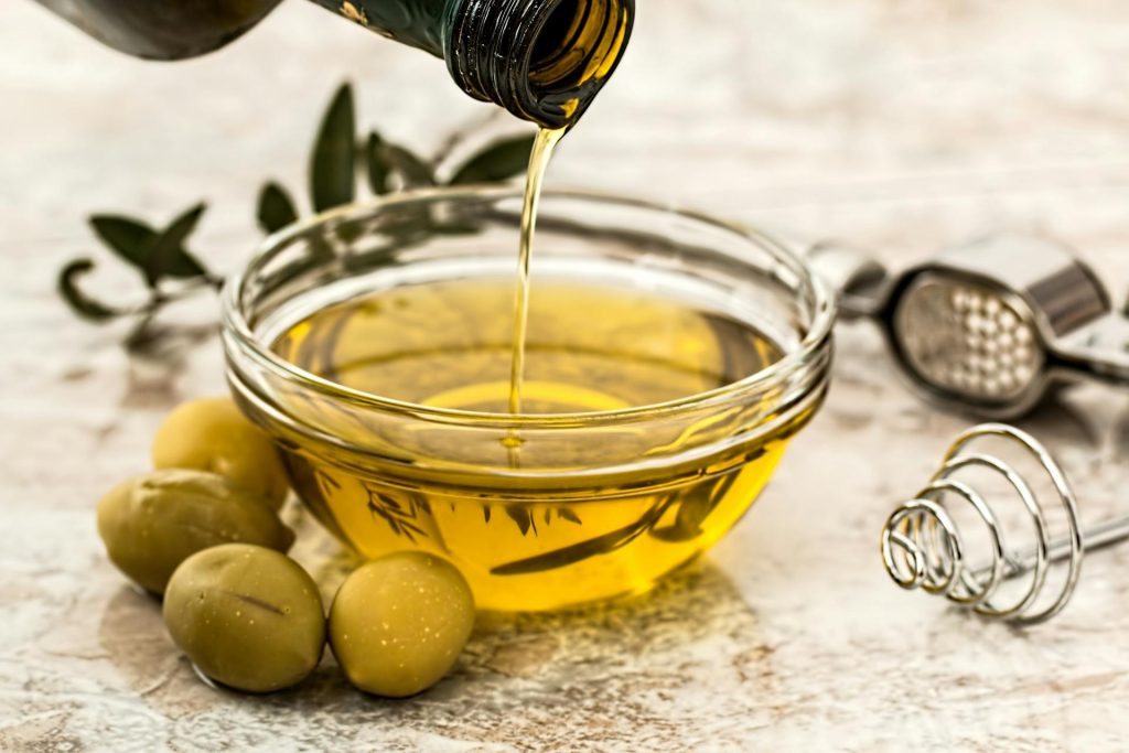 olive oil in glass bowl with olives on table