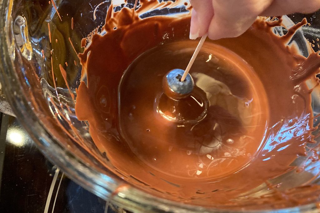 chocolate dipped blueberries on toothpick over melted chocolate