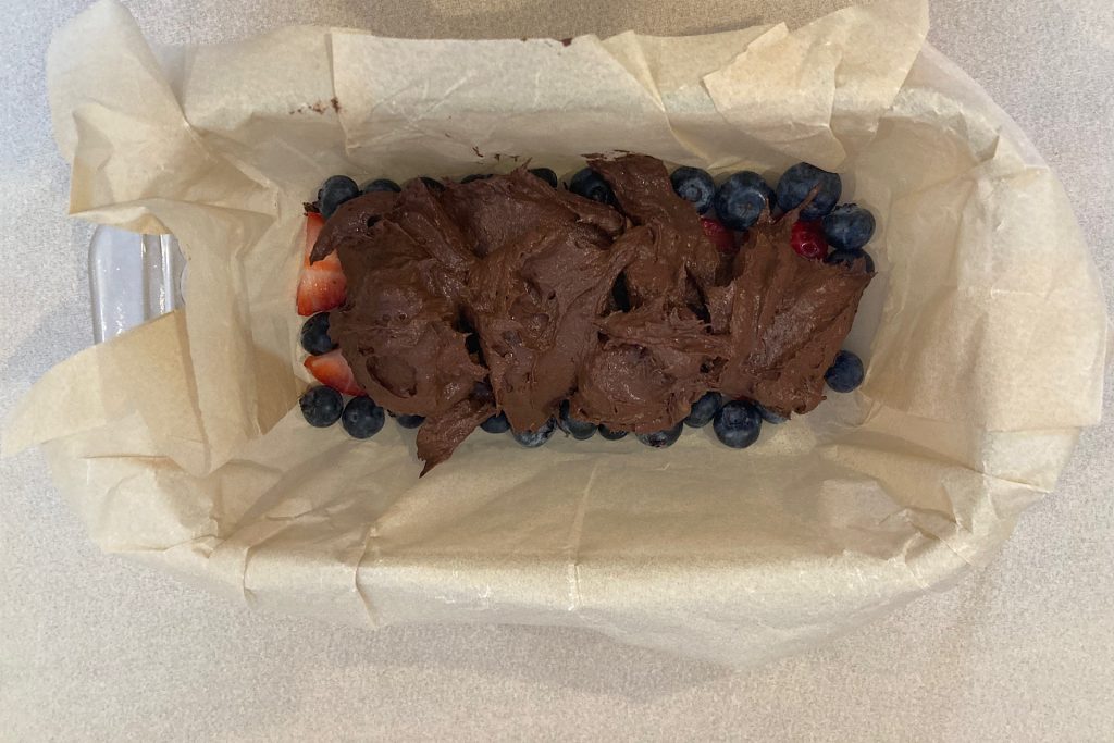 healthy no-bake chocolate banana freezer bars batter dolloped on berries in parchment-lined loaf pan