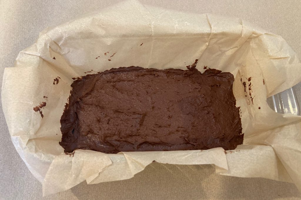 chocolate banana batter spread out in parchment-lined loaf pan