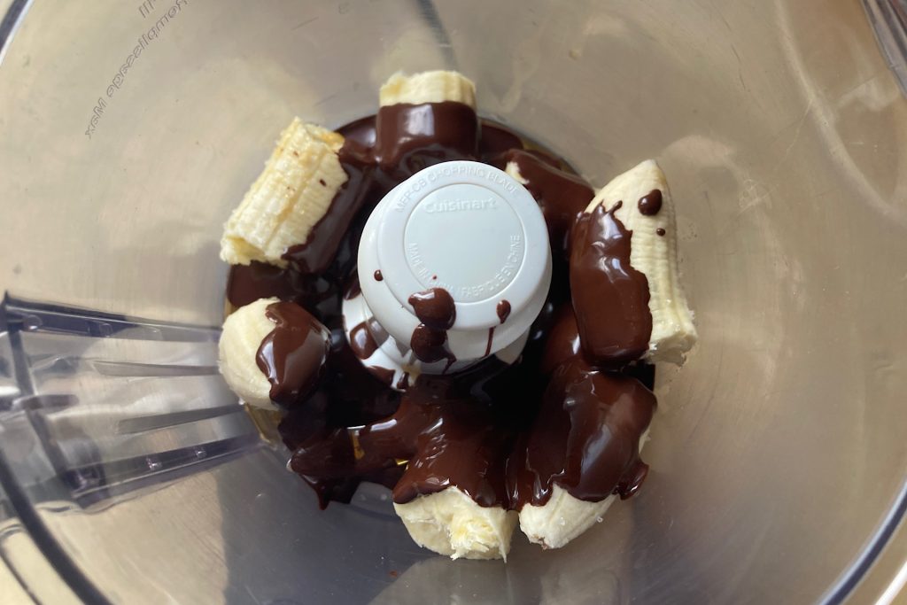 melted chocolate drizzled over bananas in food processor bowl