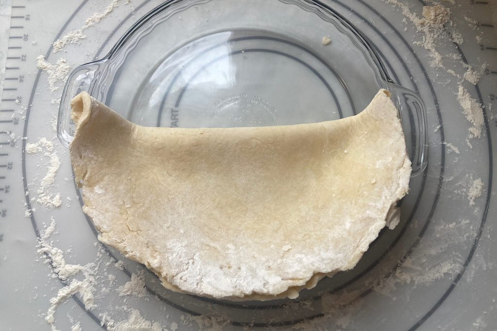 folded pie crust in Pyrex pie plate on floured mat