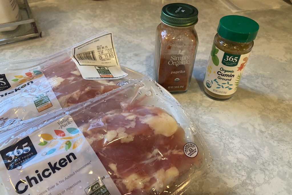 package of skinless chicken thighs, spice bottles of paprika and cumin on kitchen countertop