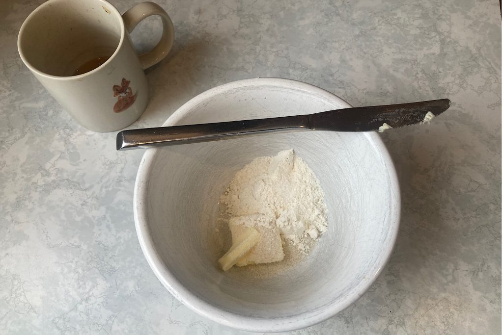 butter, sugar, flour and salt in white mixing bowl with butter knife laid on rim of bowl and coffee mug on side
