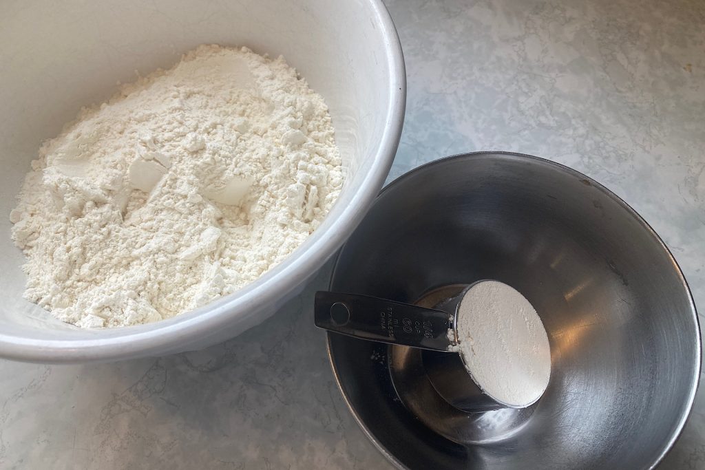Flour in white glass bowl and 1/3 cup flour in measuring cup in metal bowl