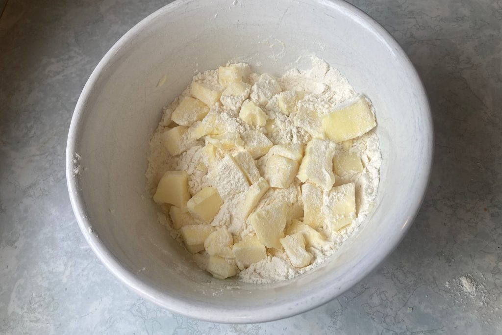 flour dusted butter slices on top of flour mound in white glass bowl