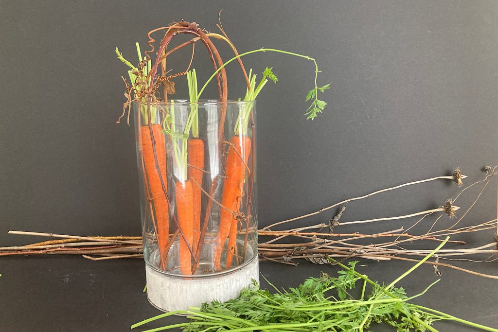 adding carrots and twigs to vase for early spring flower arrangment