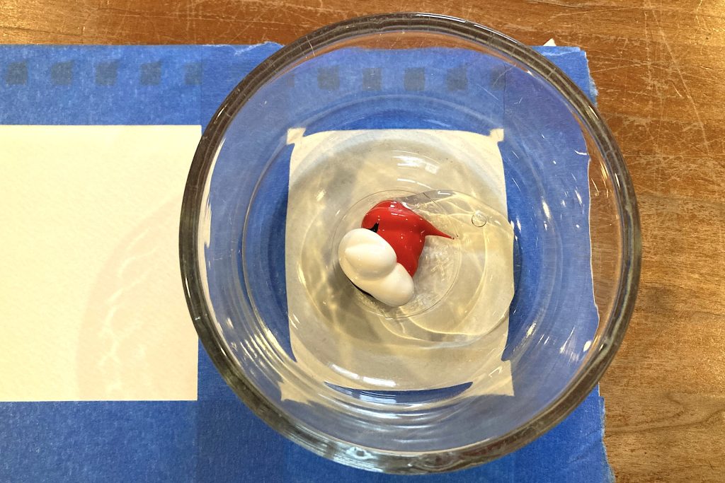 small dollop of red, white and a tinge of blue acrylic paint in a glass dish